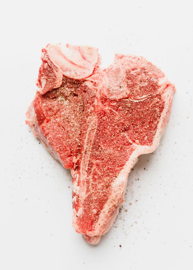 Raw t bone steak on a white cutting board