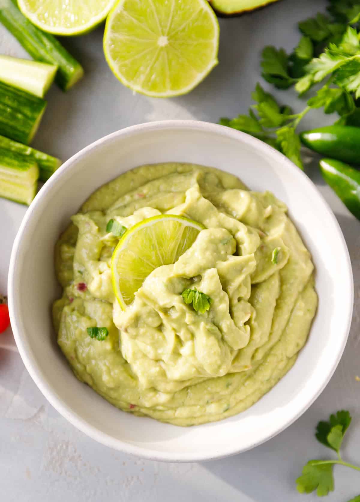 Smooth blender guacamole topped with a lime slice, surrounded by fresh limes and cilantro.