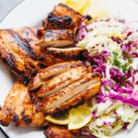Grilled chicken thighs cut and placed on a plate with cabbage salad