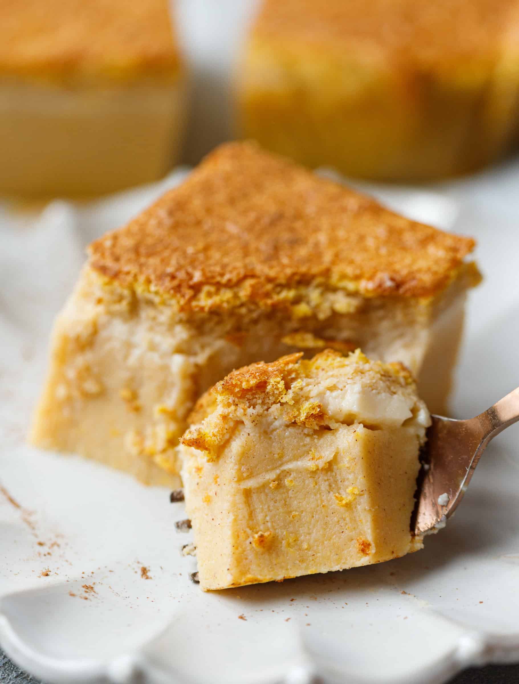 Close-up of pumpkin magic custard cake with a fork holding a bite, showing the creamy pumpkin custard layer and soft sponge top.