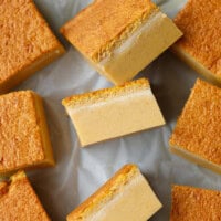 Squares of pumpkin magic custard cake on parchment paper showing distinct layers of creamy custard and soft sponge top.
