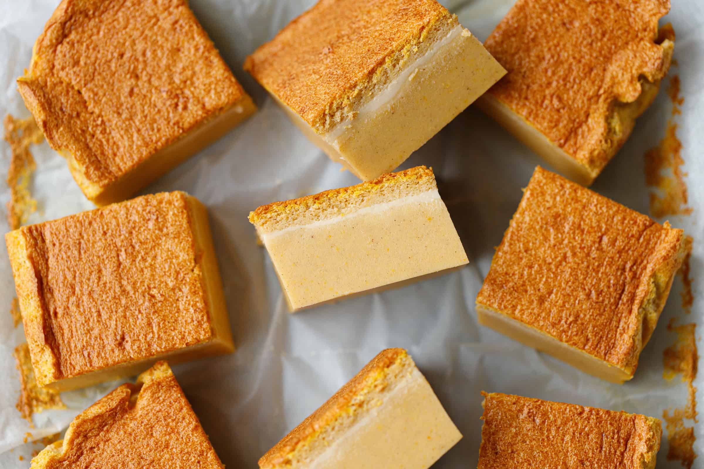 Squares of pumpkin magic custard cake on parchment paper showing distinct layers of creamy custard and soft sponge top.
