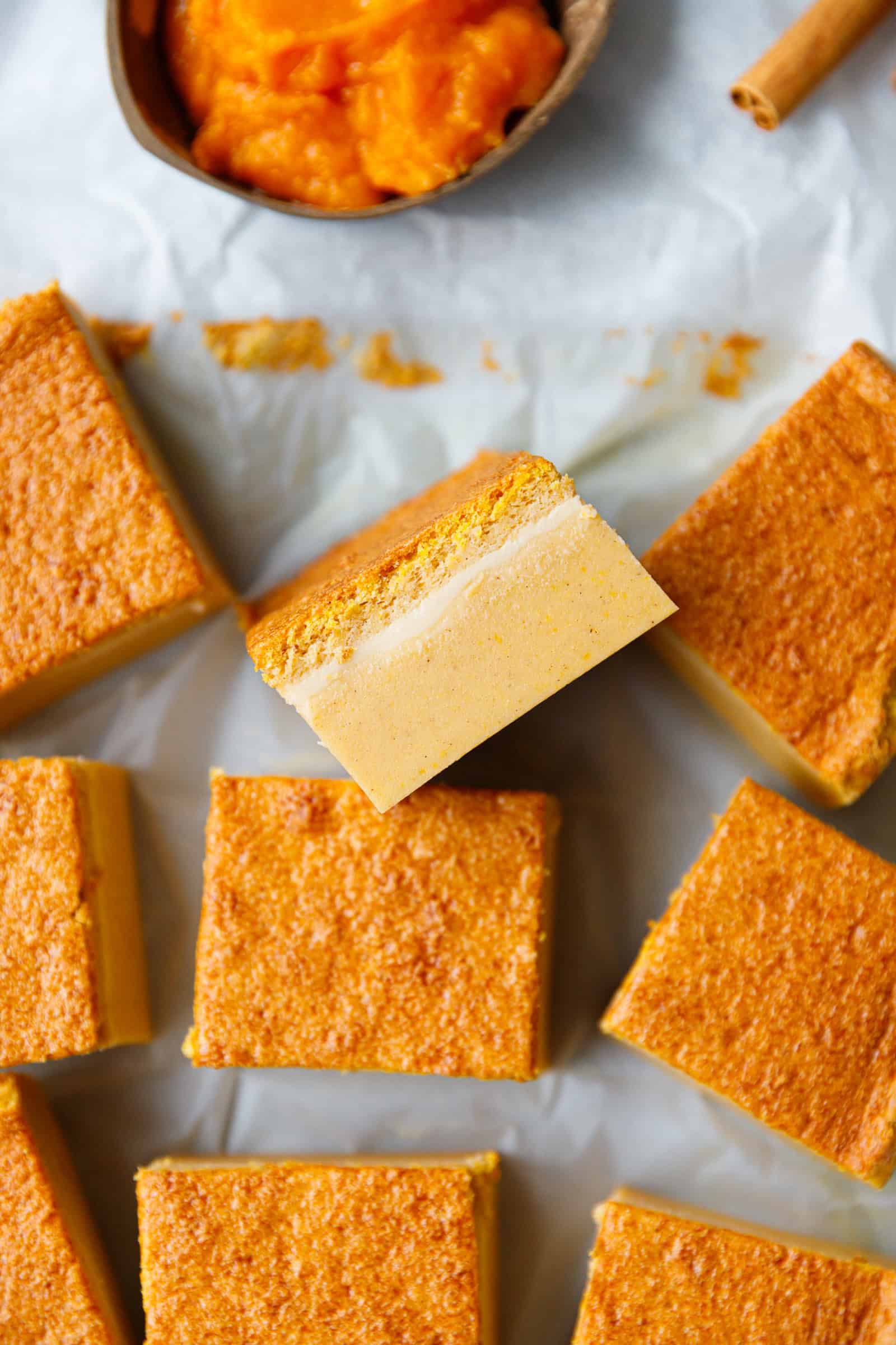 Pumpkin Magic Custard Cake Recipe – very easy to make, this cake has fall flavors and custard-like texture.  Pumpkin magic custard cake slices on parchment paper, showing three distinct layers - a soft base, creamy custard center, and golden sponge top.