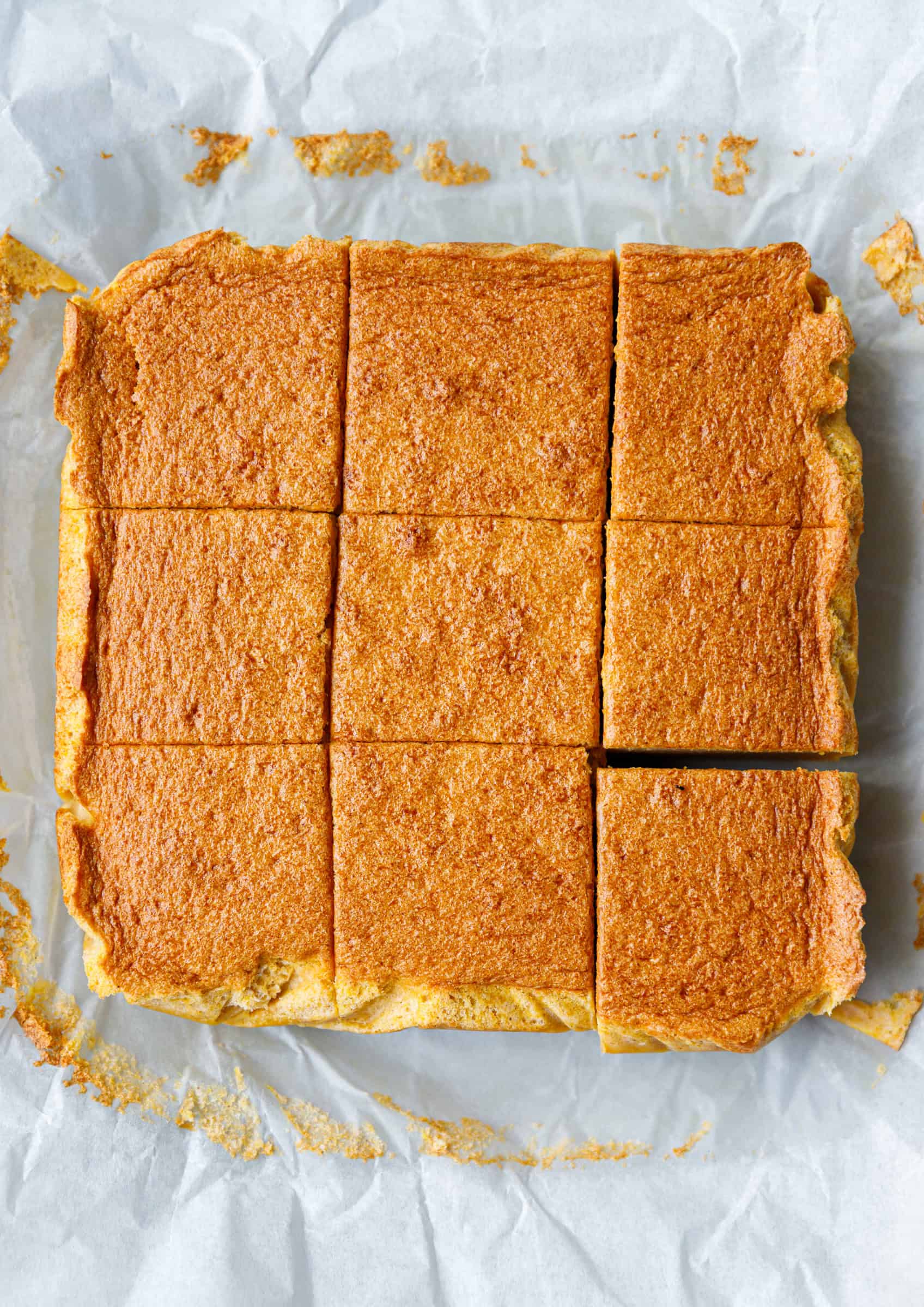 Baked pumpkin magic custard cake sliced into nine squares on parchment paper, showing a golden brown top and soft texture.