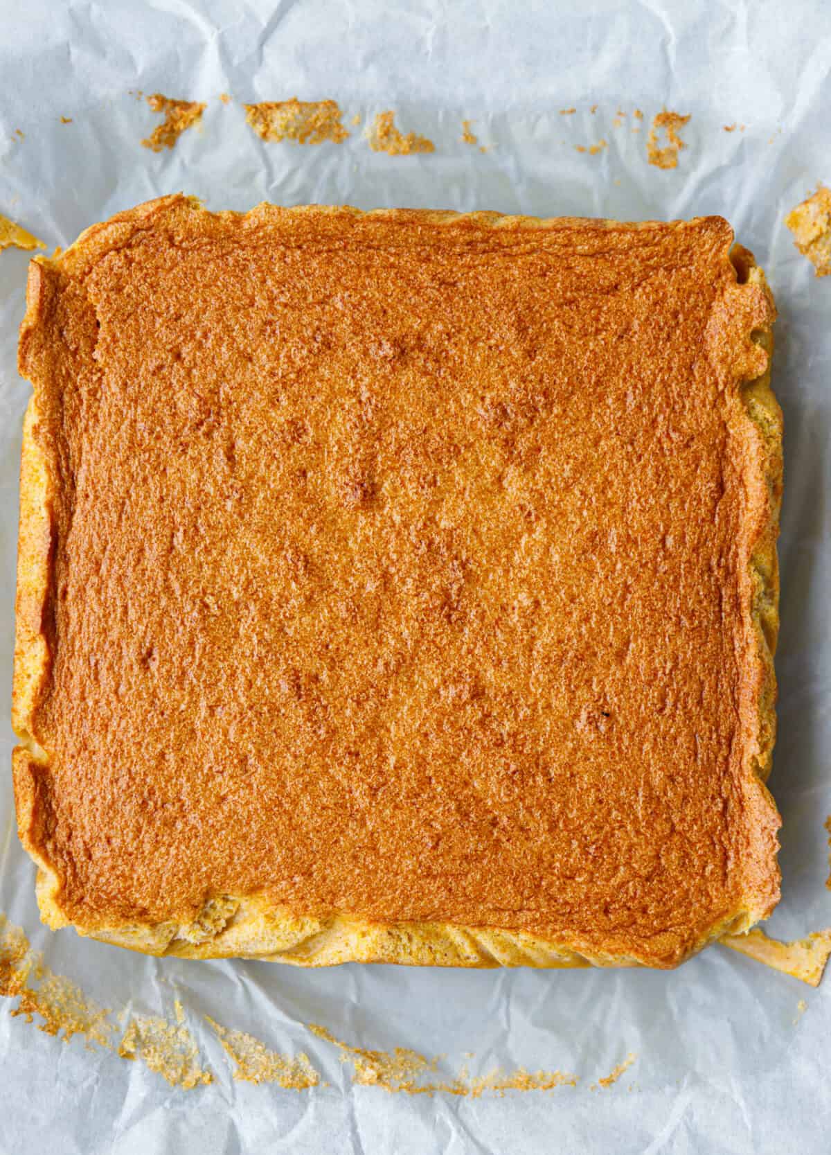 Whole pumpkin magic custard cake on parchment paper with a golden brown top, just out of the oven and ready to slice.