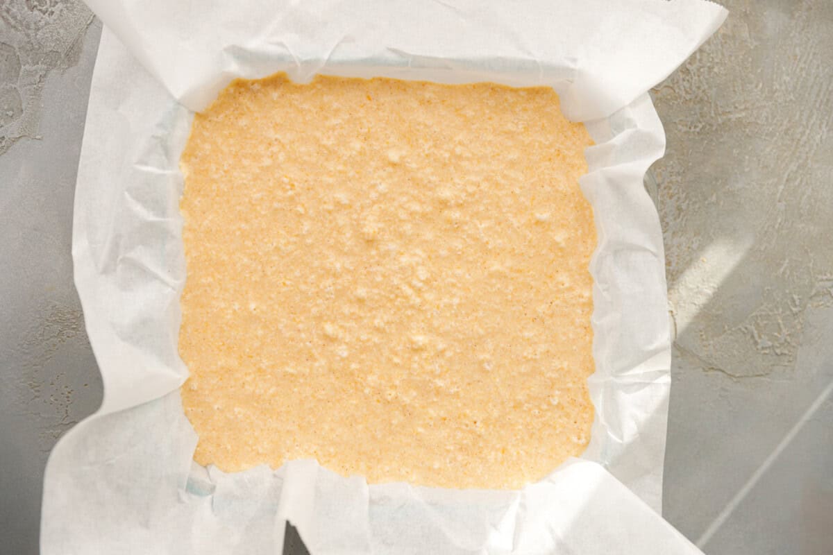 Unbaked pumpkin custard cake batter evenly spread in a parchment-lined baking pan.