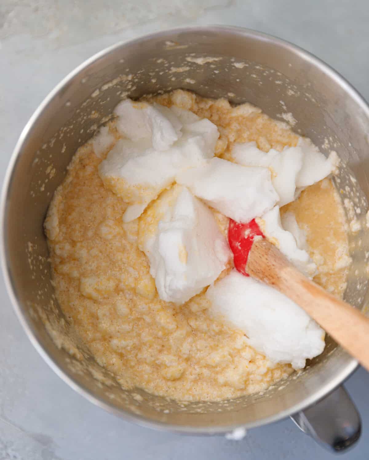 Pumpkin custard cake batter partially mixed with whipped egg whites using a red spatula.