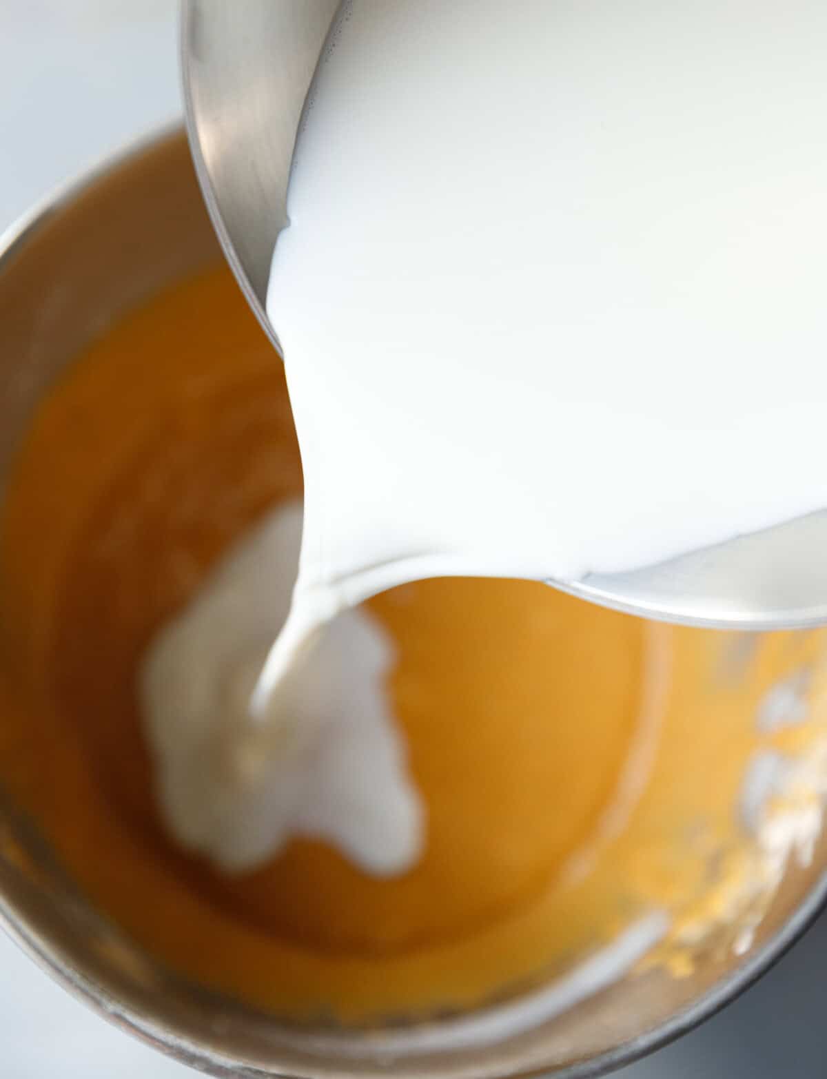 Warm milk being poured into pumpkin custard cake batter in a mixing bowl.