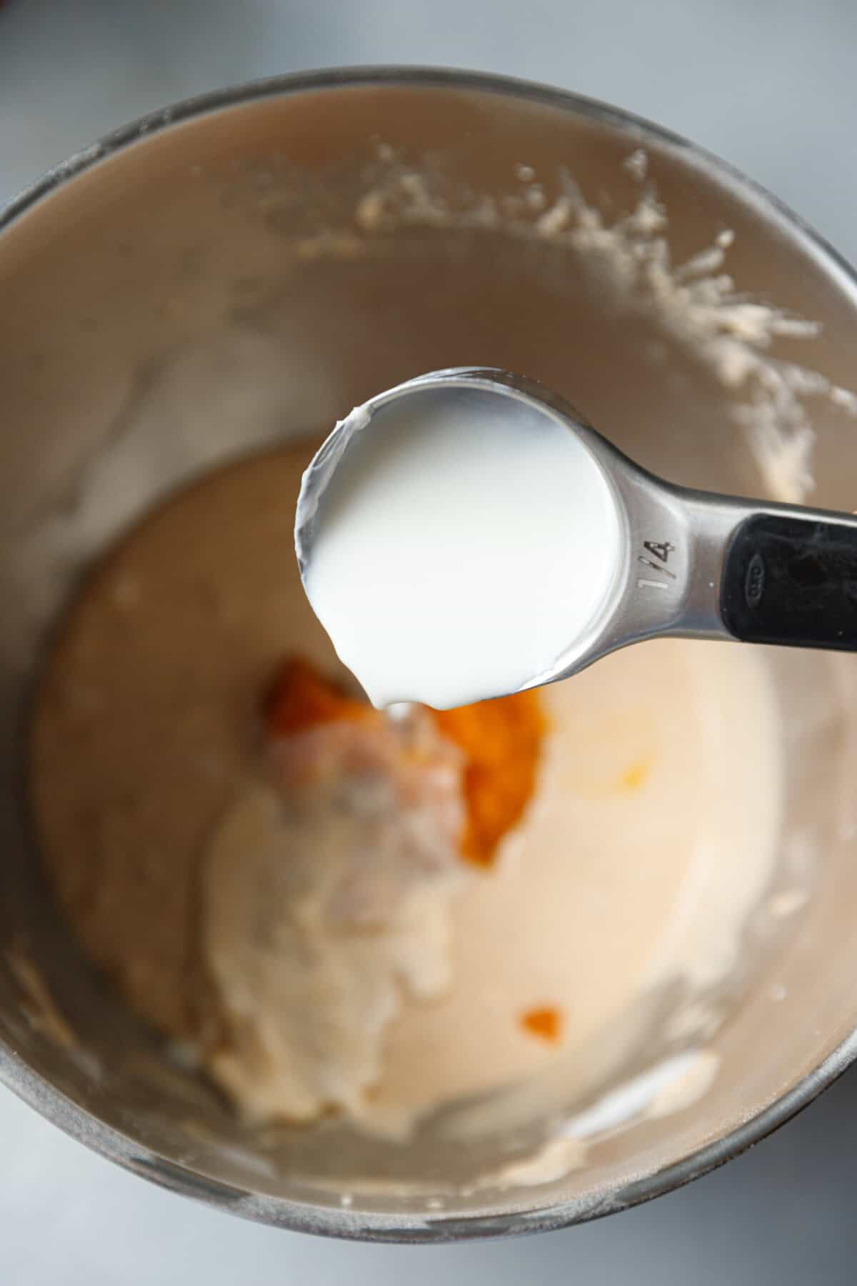 Pouring a quarter cup of milk into pumpkin custard cake batter to loosen the mixture before adding the rest of the milk.