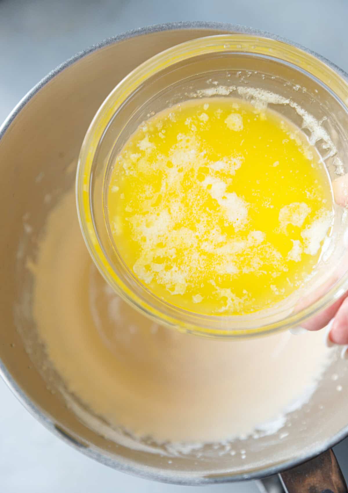Melted butter being poured into whipped egg yolk mixture to create the rich batter for pumpkin magic custard cake.