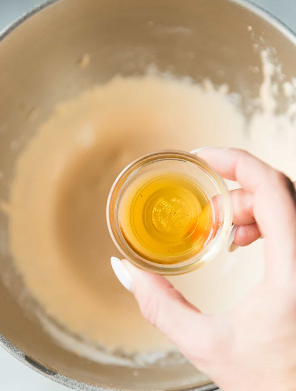 Hand holding a small bowl of vanilla extract over whipped egg yolk mixture for pumpkin magic custard cake batter.