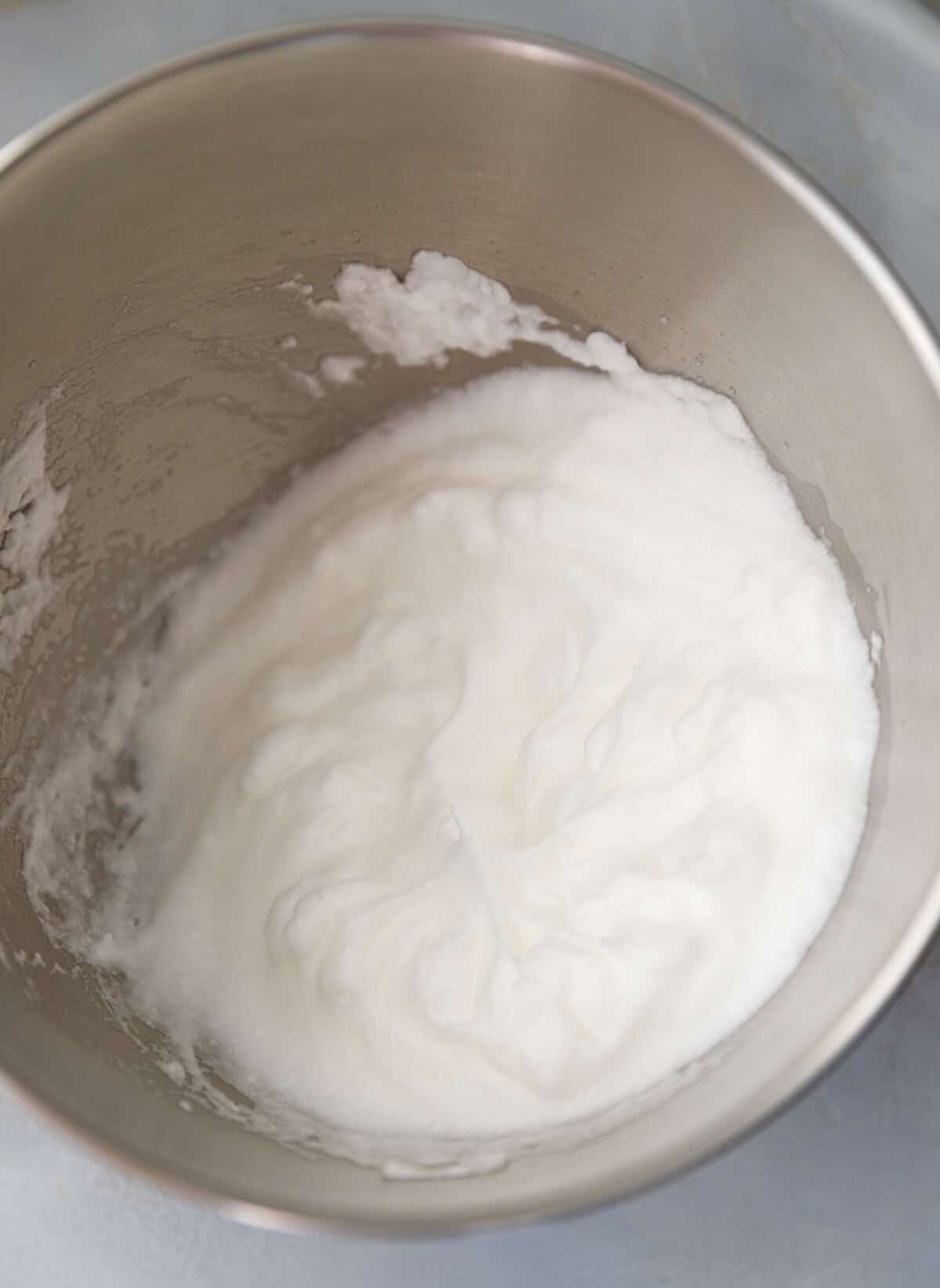 Bowl of stiffly whipped egg whites with smooth peaks, ready to be folded into pumpkin custard cake batter.