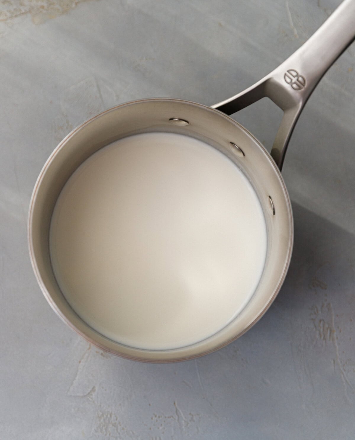 Warm milk in a stainless steel saucepan on a gray surface, prepared for making pumpkin magic custard cake batter.