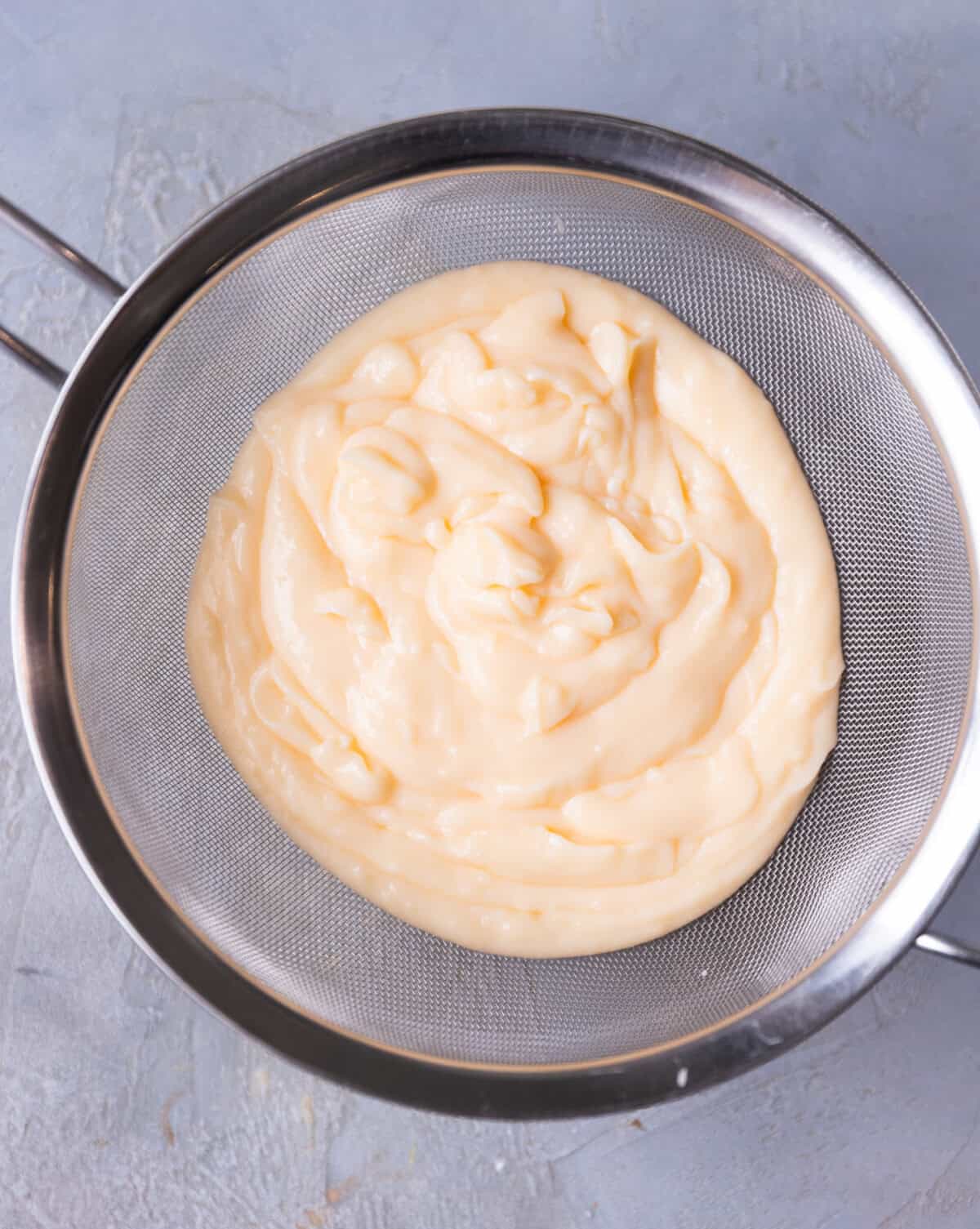 A fine mesh strainer over a glass bowl to strain egg custard