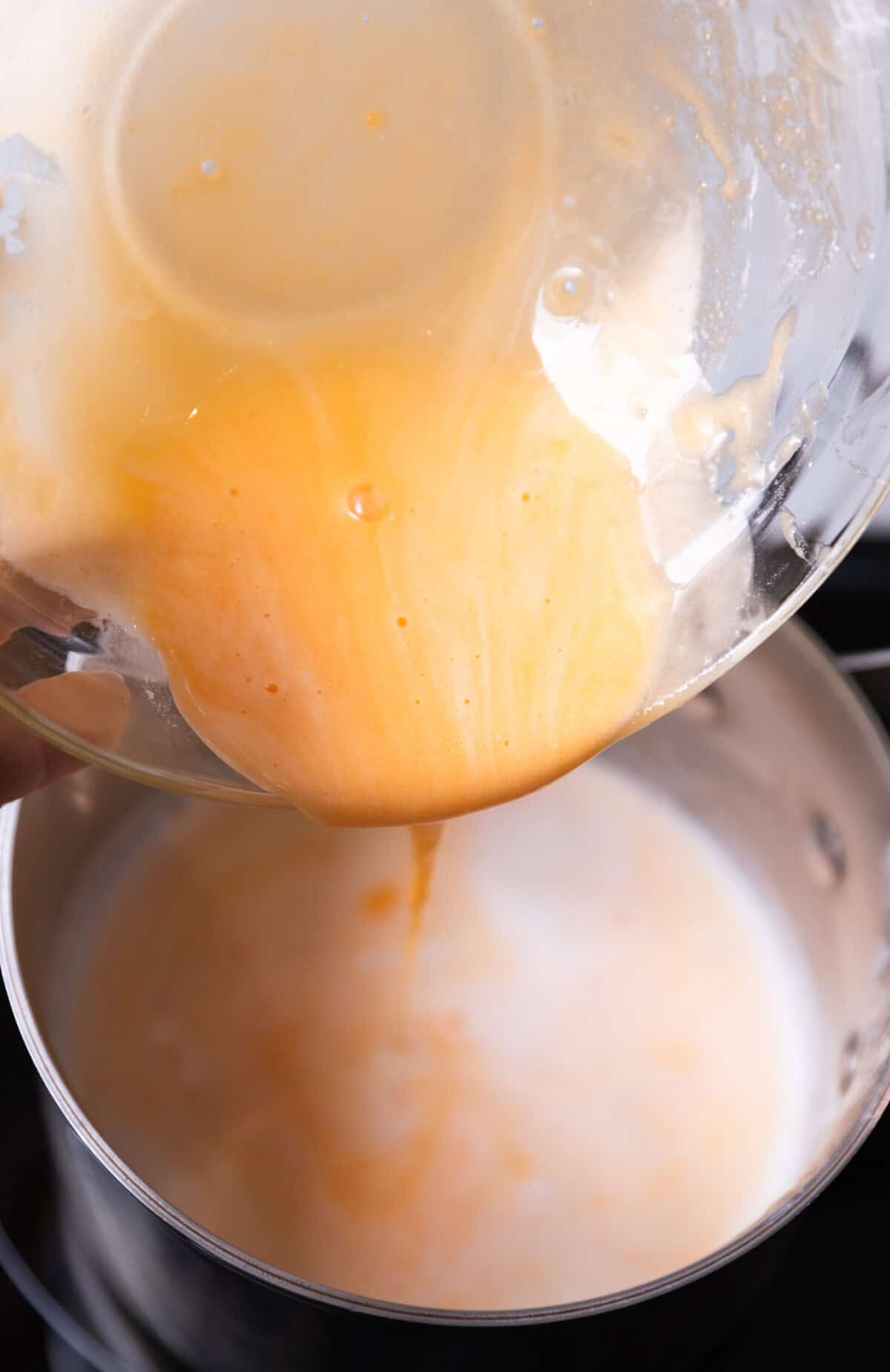 A saucepan with warm milk and sugar on a stove top and a mixture of egg yolks, sugar and cornstarch poured inside