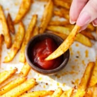 Hand dipping a crispy baked oven fry into a small bowl of ketchup.