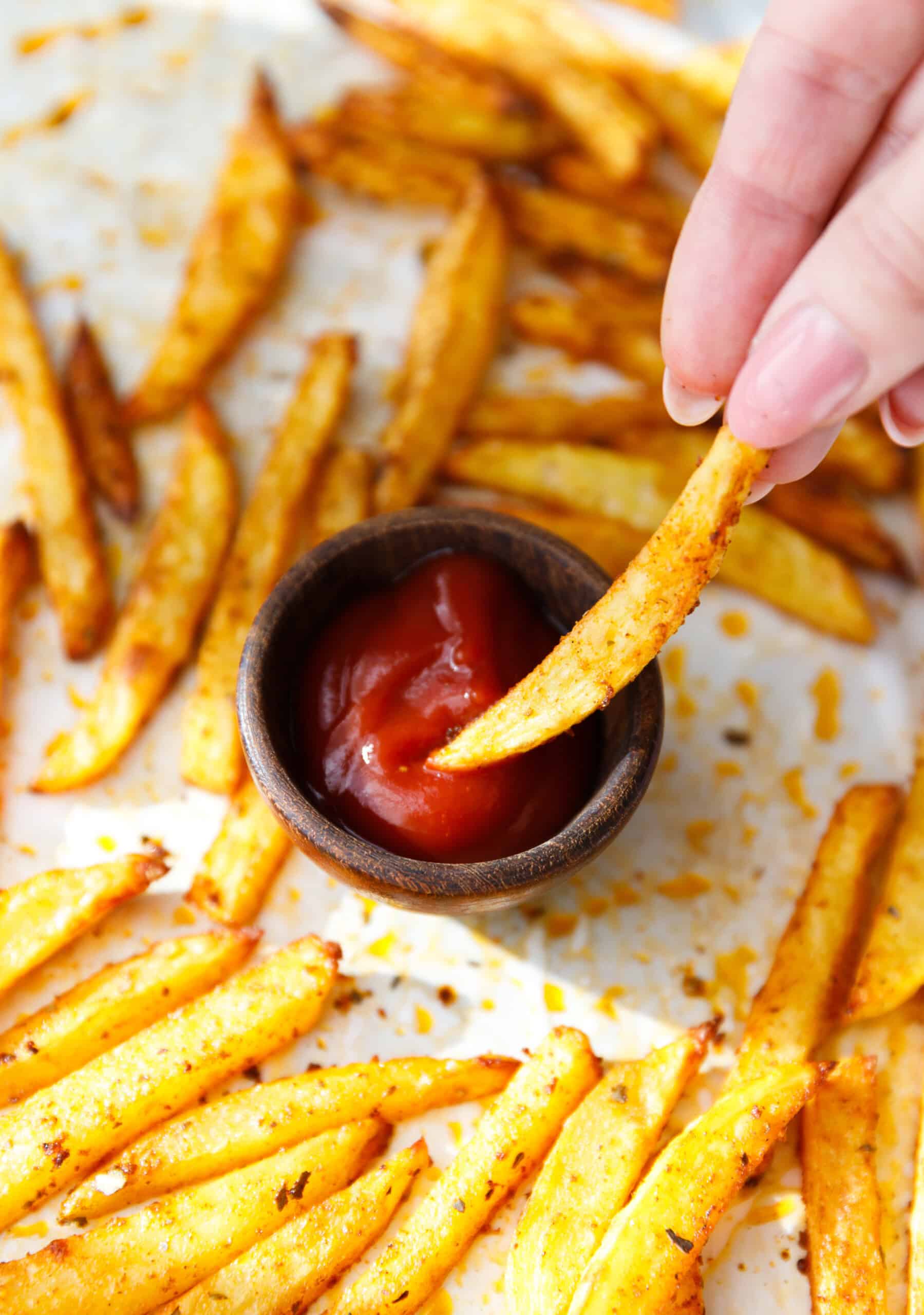 Hand dipping a crispy baked oven fry into a small bowl of ketchup.