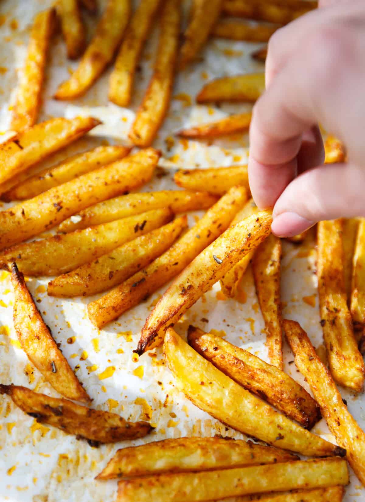 Hand picking up a crispy baked oven fry from a sheet pan.