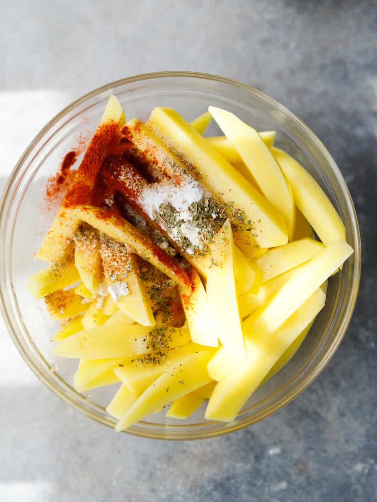 Russet potatoes, oil and seasonings arranged on a countertop for oven fries.
