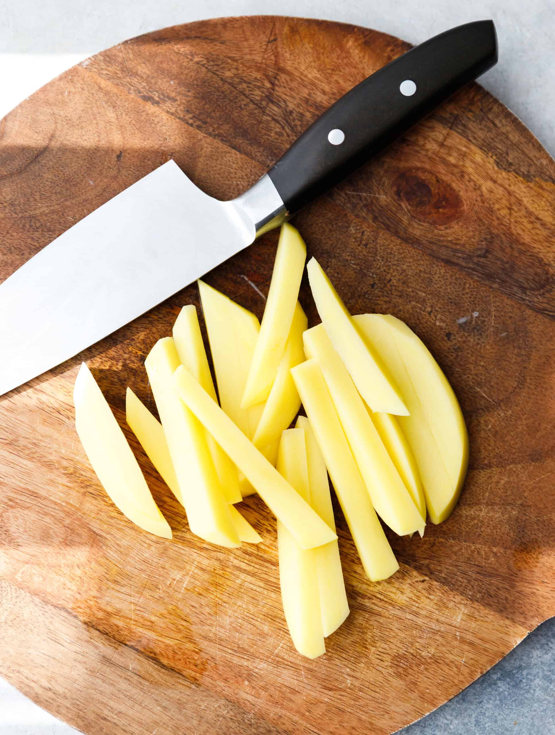 Hand-cut potato matchsticks on a wooden cutting board with a chef’s knife.