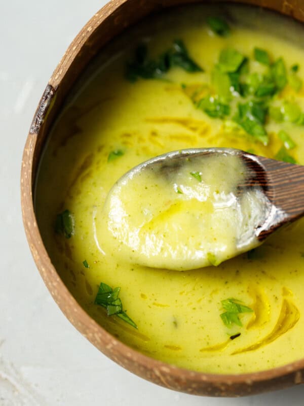 Creamy zucchini soup served in a coconut bowl, topped with fresh parsley and olive oil, with a spoon lifting a smooth bite.