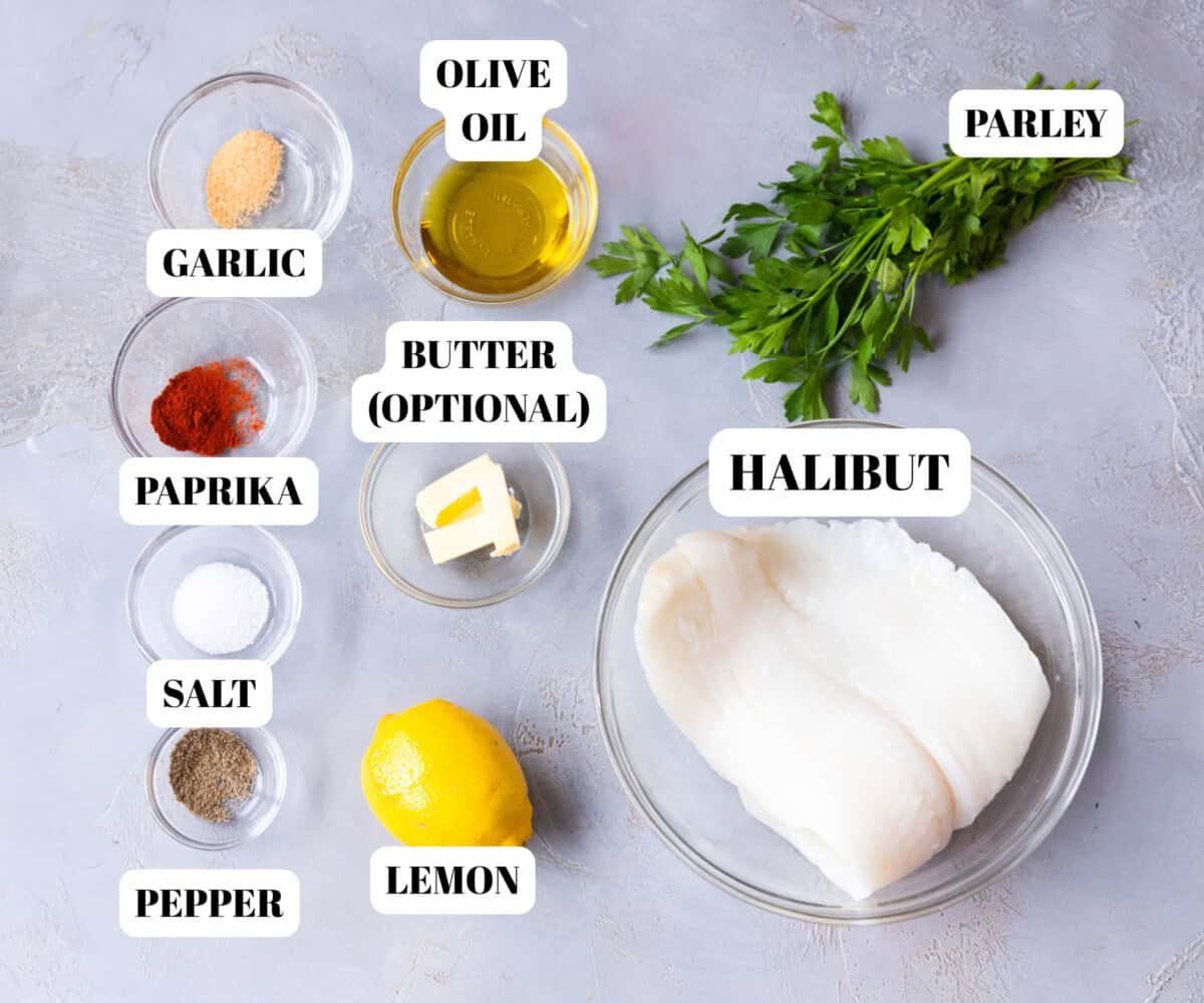 Ingredients for baked halibut recipe including fresh halibut fillets, olive oil, butter, lemon, garlic, paprika, salt, and pepper arranged on a table.