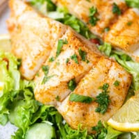 Baked halibut fillet served on top of a fresh green salad with lemon wedge