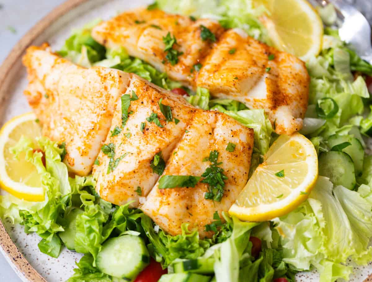 Overhead shot of baked halibut fillets with golden edges and fresh herbs