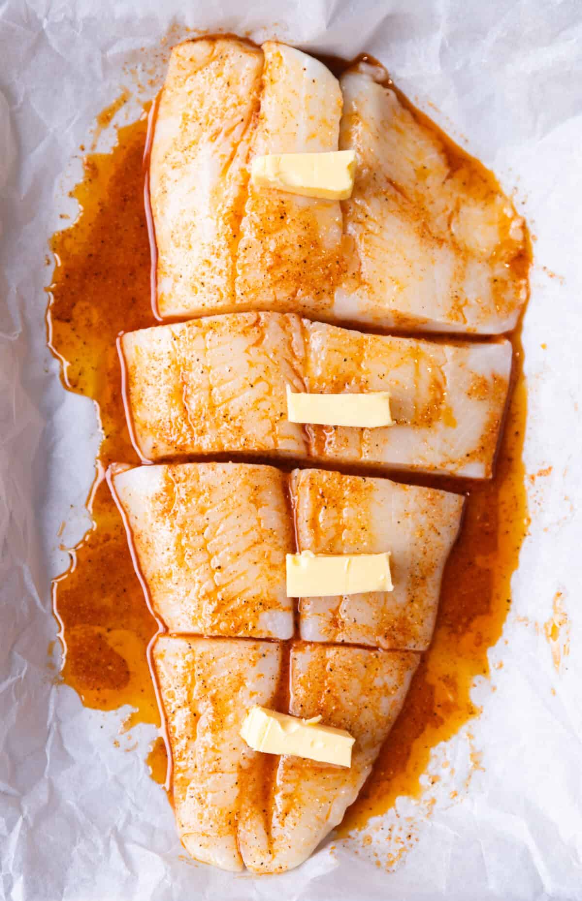 Halibut fillets arranged in a parchment-lined baking dish, ready for the oven topped with butter.