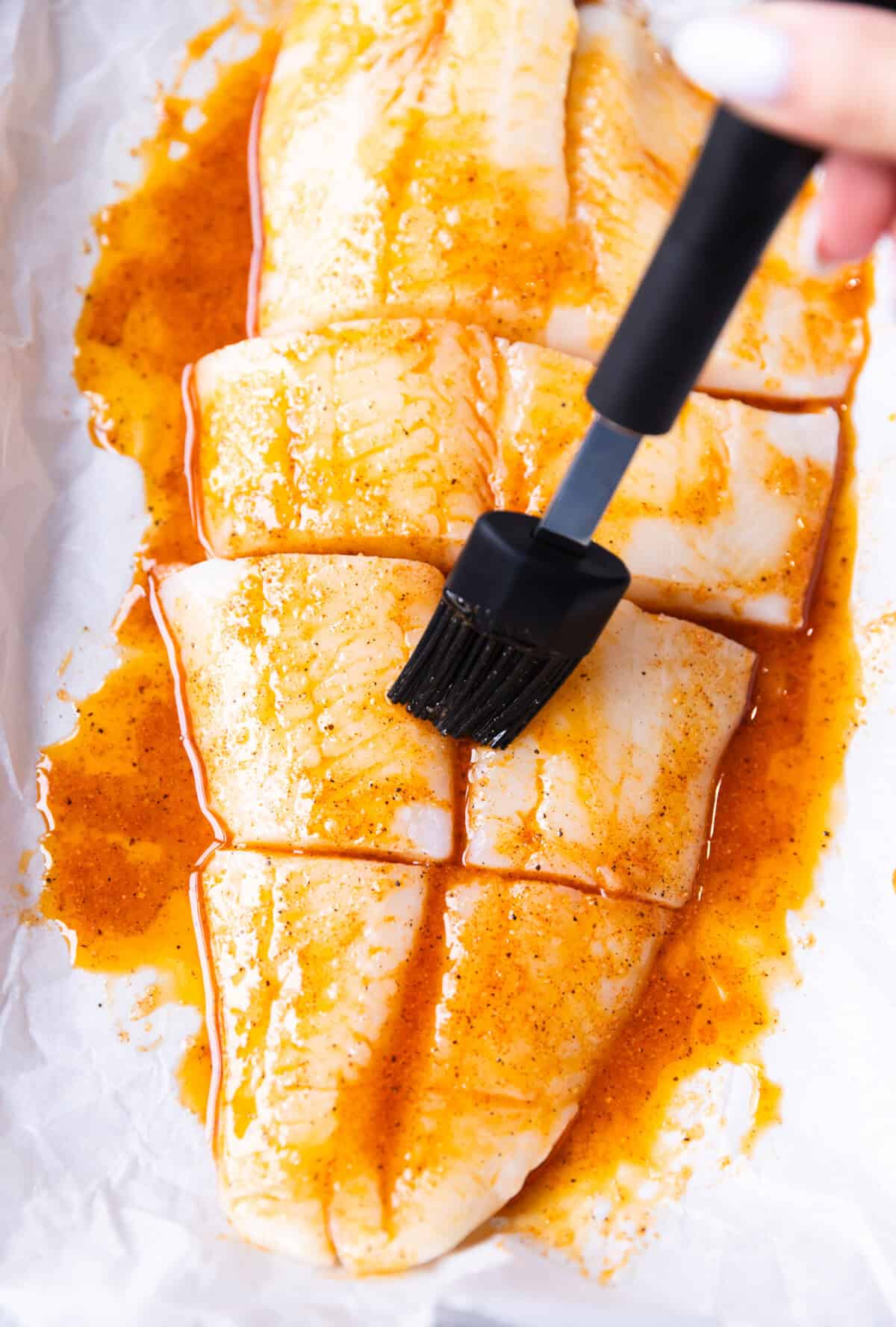 Brushing halibut fillets with garlic butter mixture in a baking dish