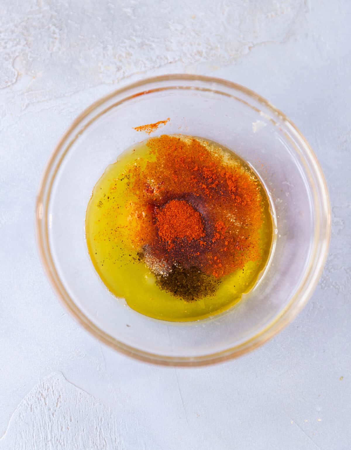 A small glass bowl with olive oil, lemon juice and spices before being whisked.