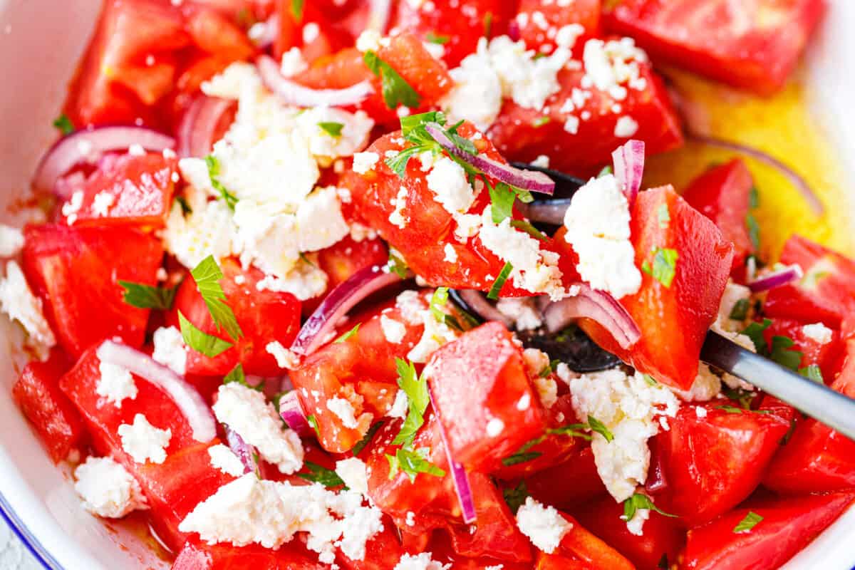 Close-up of Bulgarian tomato salad with feta, red onion, and parsley on a fork