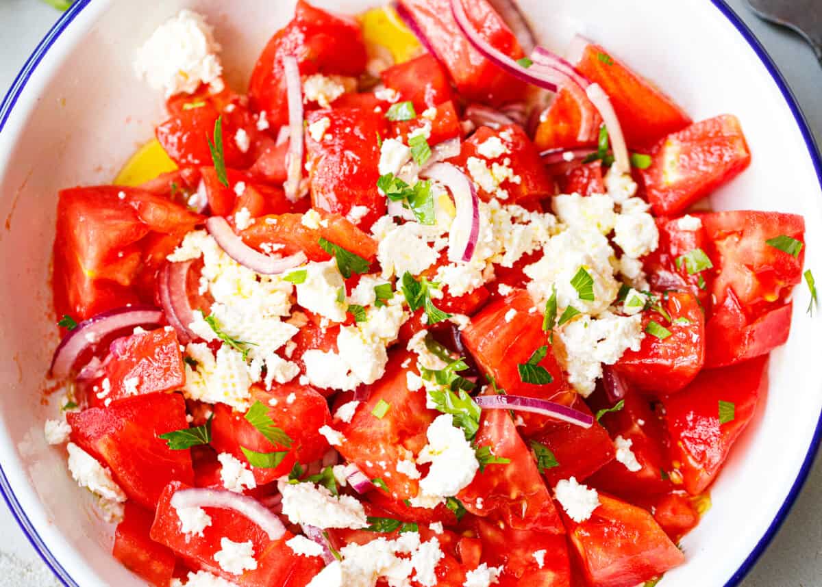 Bulgarian tomato salad with crumbled feta, red onion, and parsley in a blue-rimmed bowl