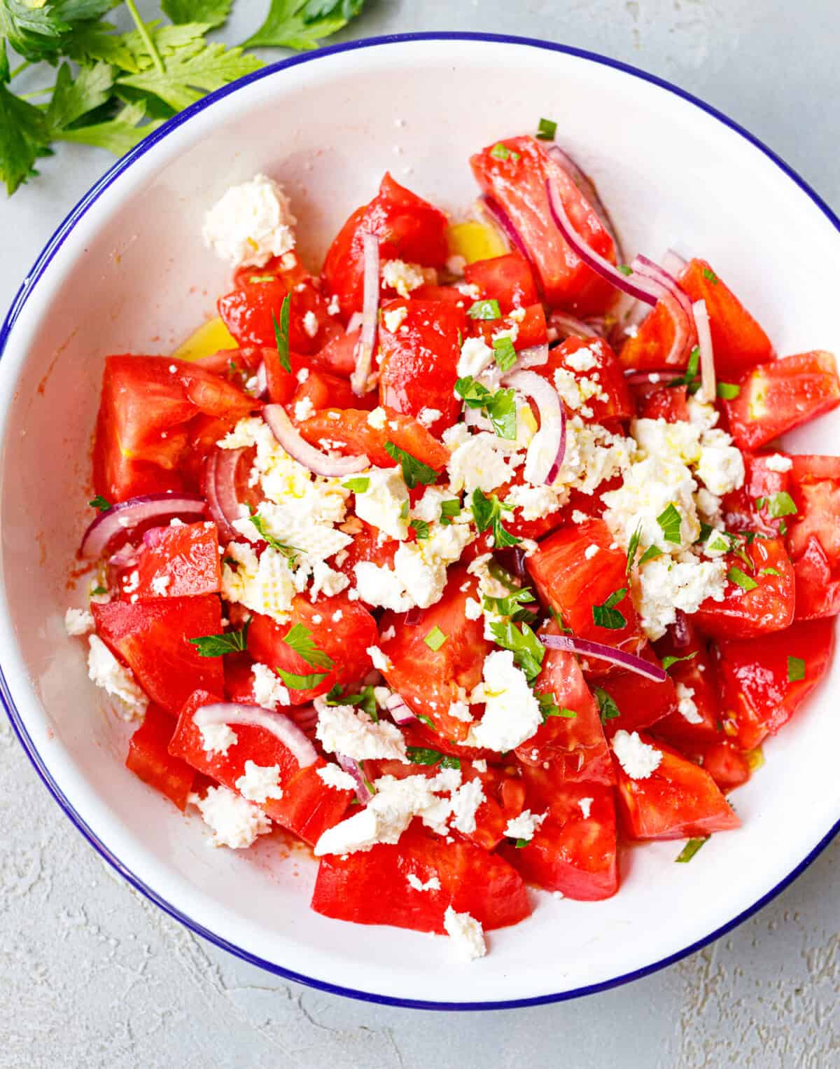 Overhead bowl of tomato salad with feta, red onion, and fresh parsley