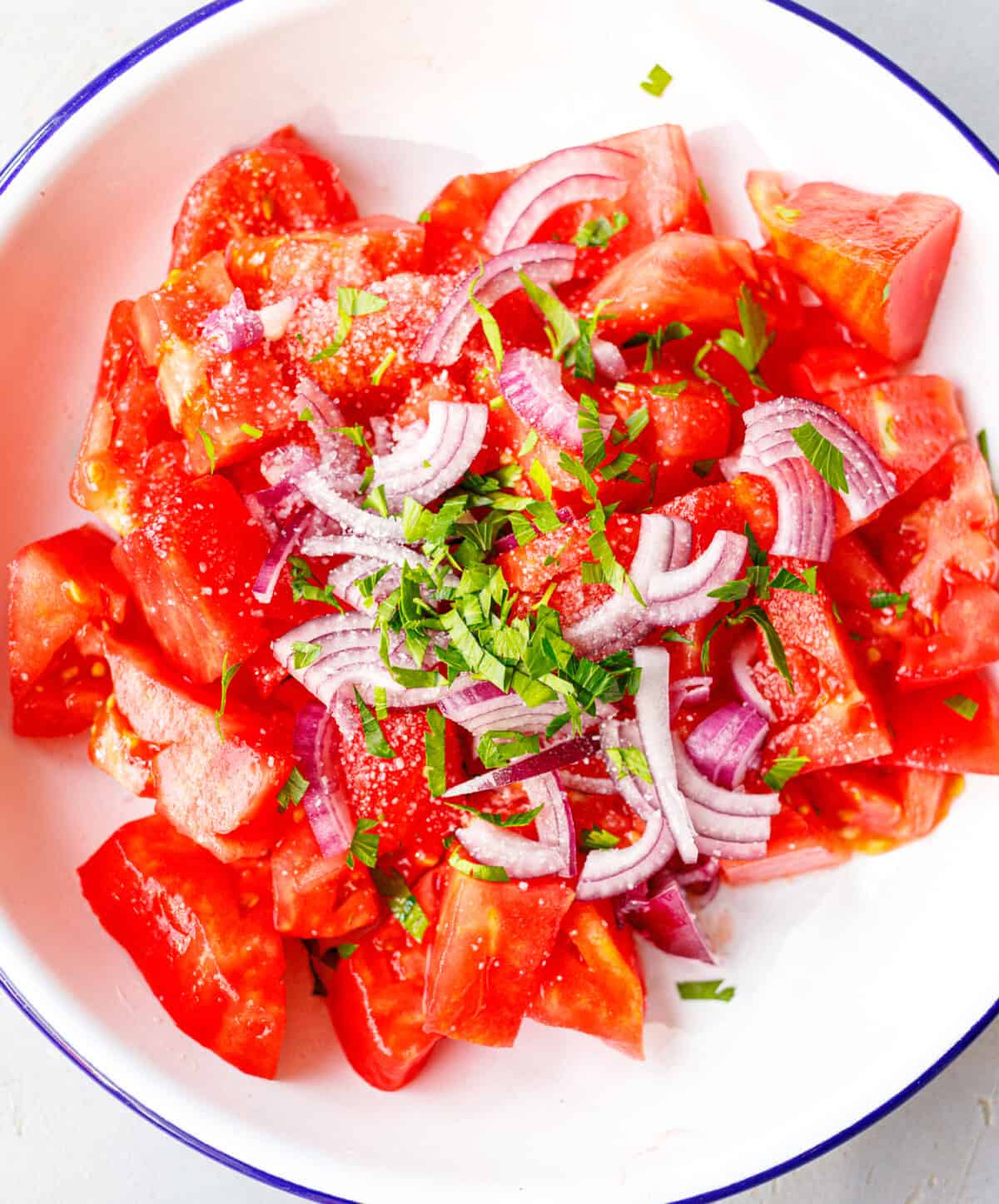 Chopped tomatoes with red onion, parsley, and salt in a white bowl before adding feta
