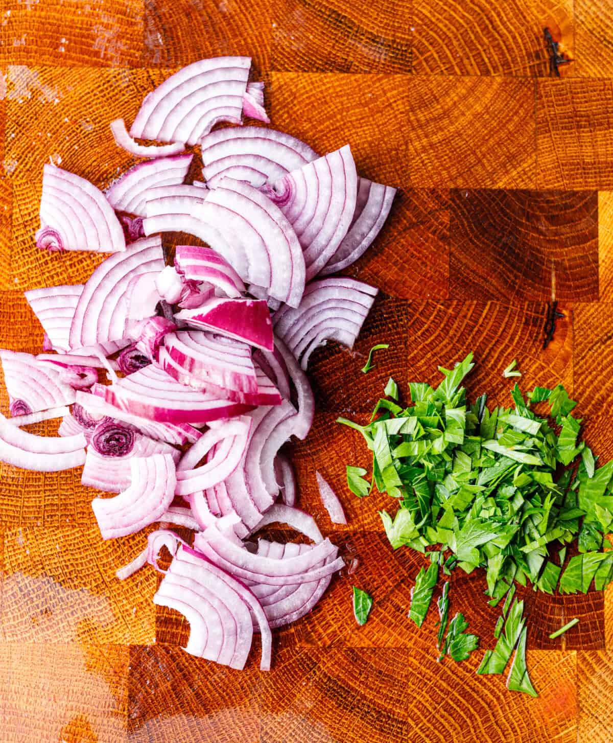 Thinly sliced red onion and chopped parsley on a wooden board for tomato salad