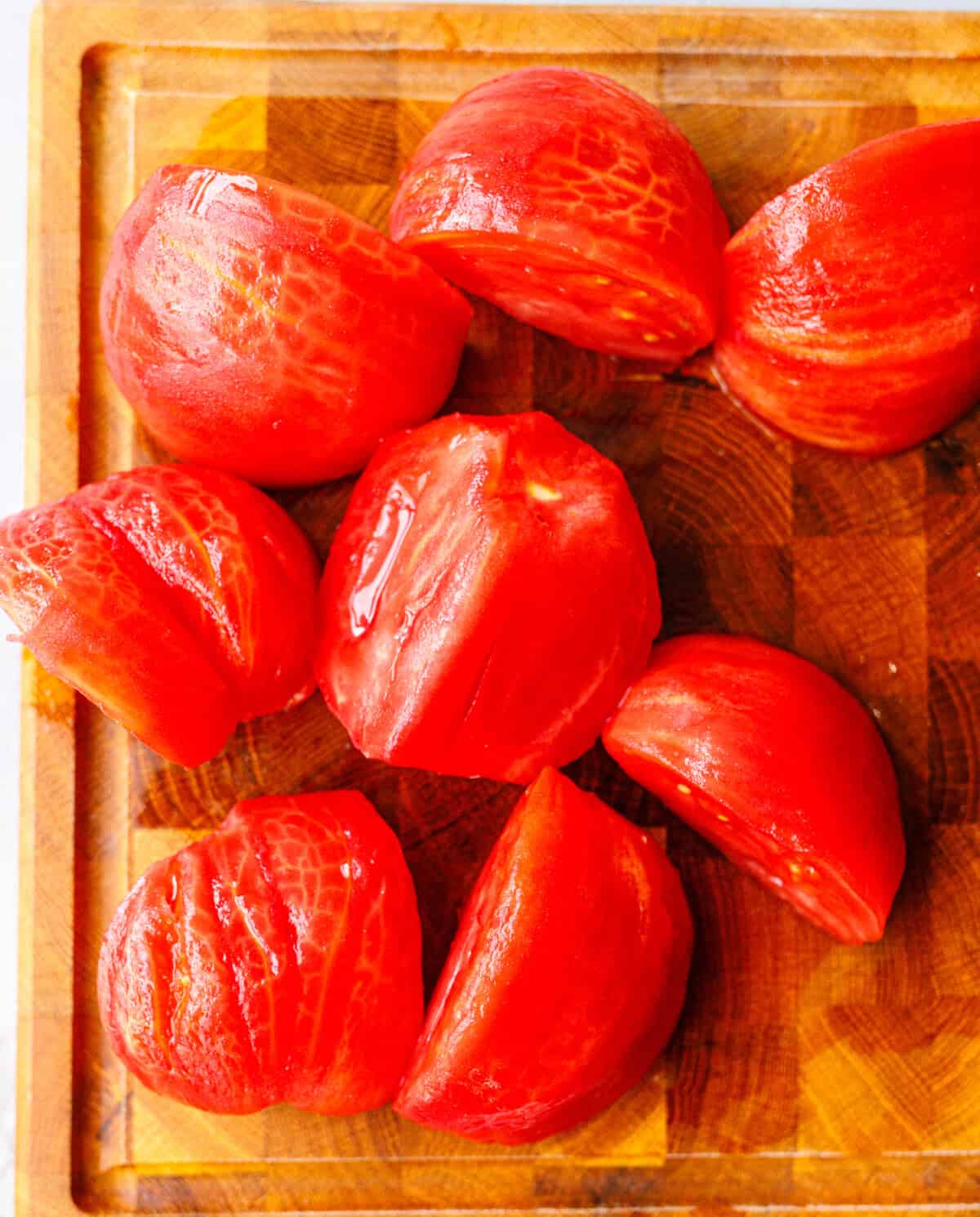 Peeled quartered tomatoes on a wooden cutting board, ready to chop for tomato salad