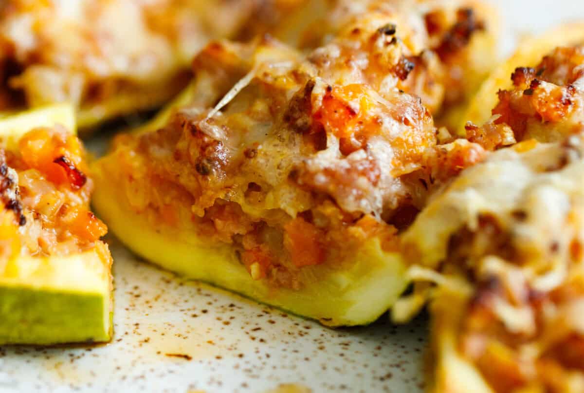 Cut end of a stuffed zucchini boat showing the ground beef, carrot, and tomato filling with melted cheese on top