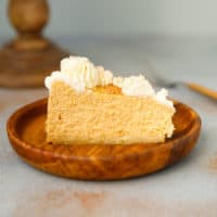 A slice of low carb pumpkin cheesecake with whipped cream on a wooden plate