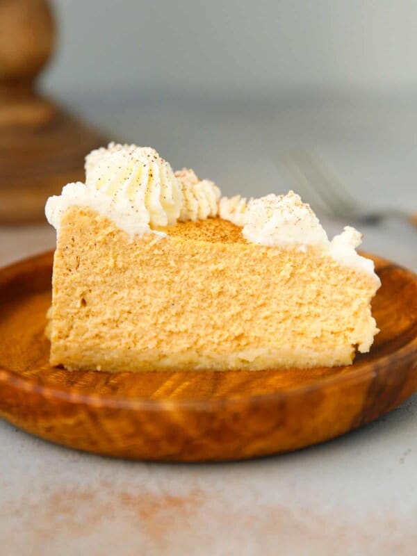 A slice of low carb pumpkin cheesecake with whipped cream on a wooden plate