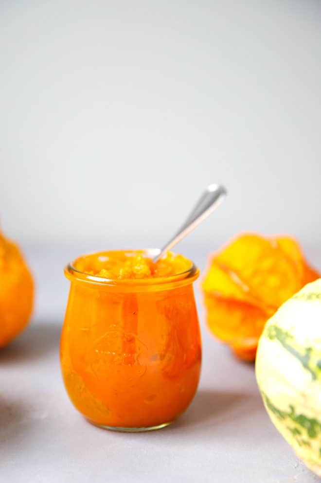 Pumpkin puree in a glass jar with decorative pumpkins around it