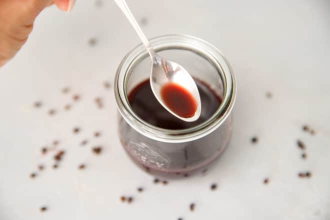A Weck jar filled with elderberry syrup and a spoon spooning it out