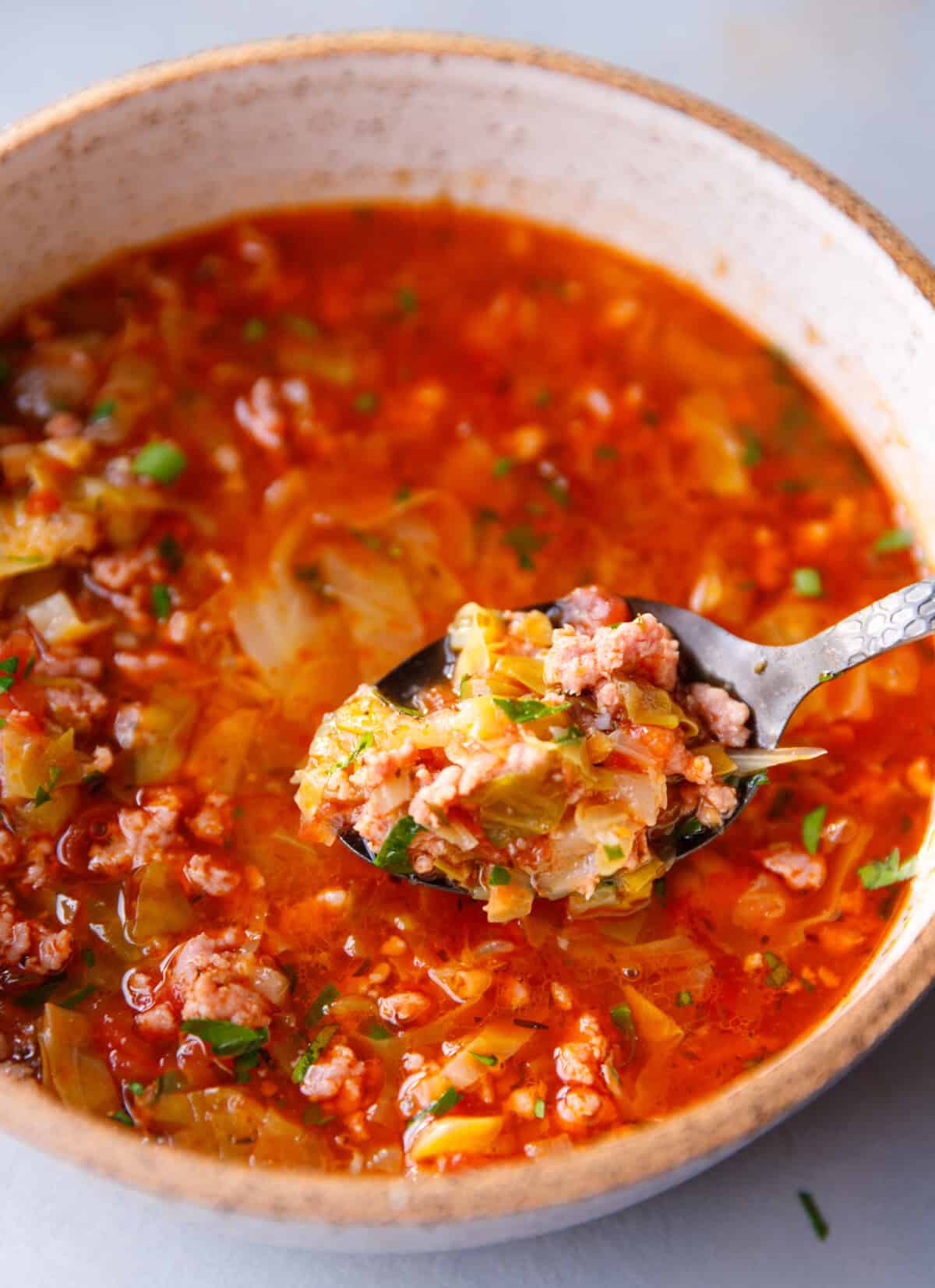 Close-up of Keto Cabbage Roll Soup in a bowl, with a spoon lifting tender cabbage, ground beef, and tomato broth — a hearty low-carb, high-protein soup perfect for cozy dinners.