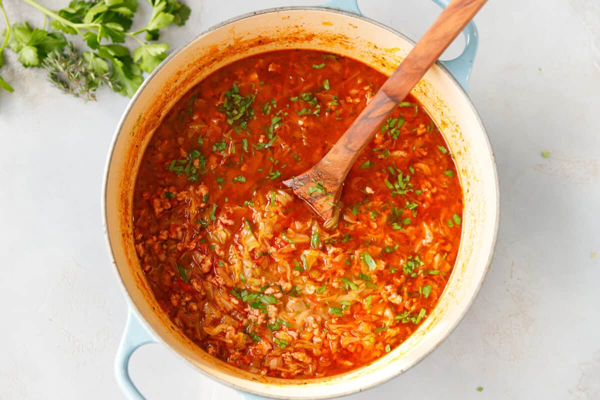 Large Dutch oven filled with Keto Cabbage Roll Soup made with ground beef, cabbage, and tomatoes, garnished with parsley - easy one-pot keto soup for meal prep.