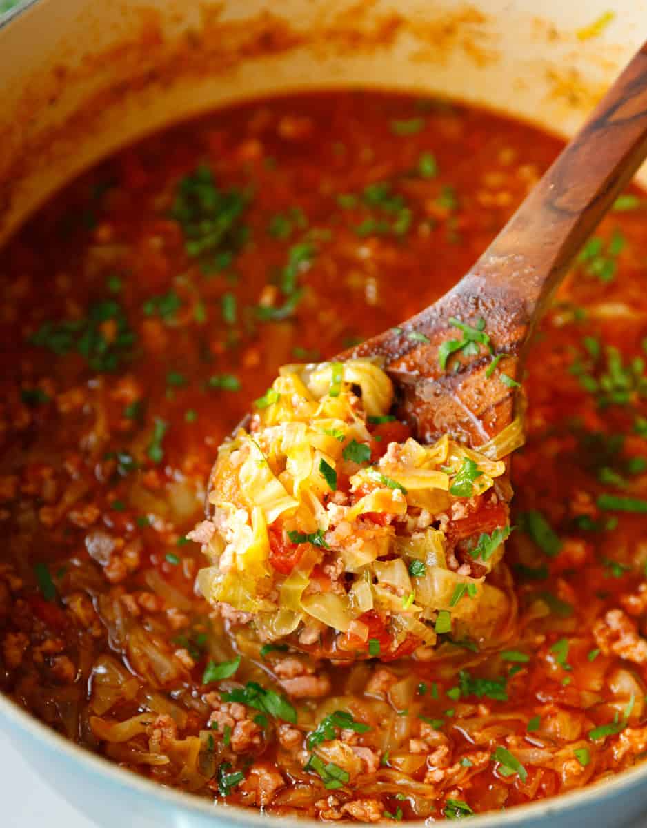 A Dutch oven with chunky cabbage soup and a wooden ladle scooping out of it.