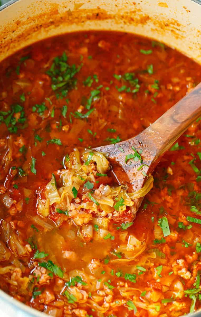 A wooden spoon scooping out cabbage soup from a pot.