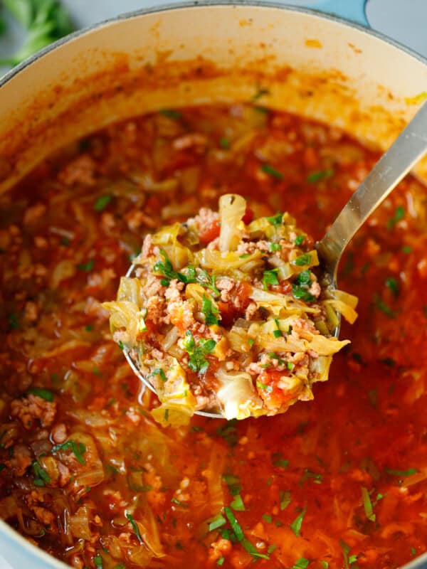 Ladle of Keto Cabbage Roll Soup in a Dutch oven filled with tender cabbage, ground beef, and tomatoes in a rich, flavorful broth - hearty low-carb soup perfect for meal prep.
