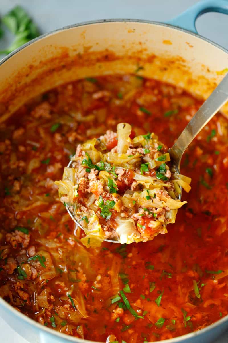 Ladle of Keto Cabbage Roll Soup in a Dutch oven filled with tender cabbage, ground beef, and tomatoes in a rich, flavorful broth - hearty low-carb soup perfect for meal prep.