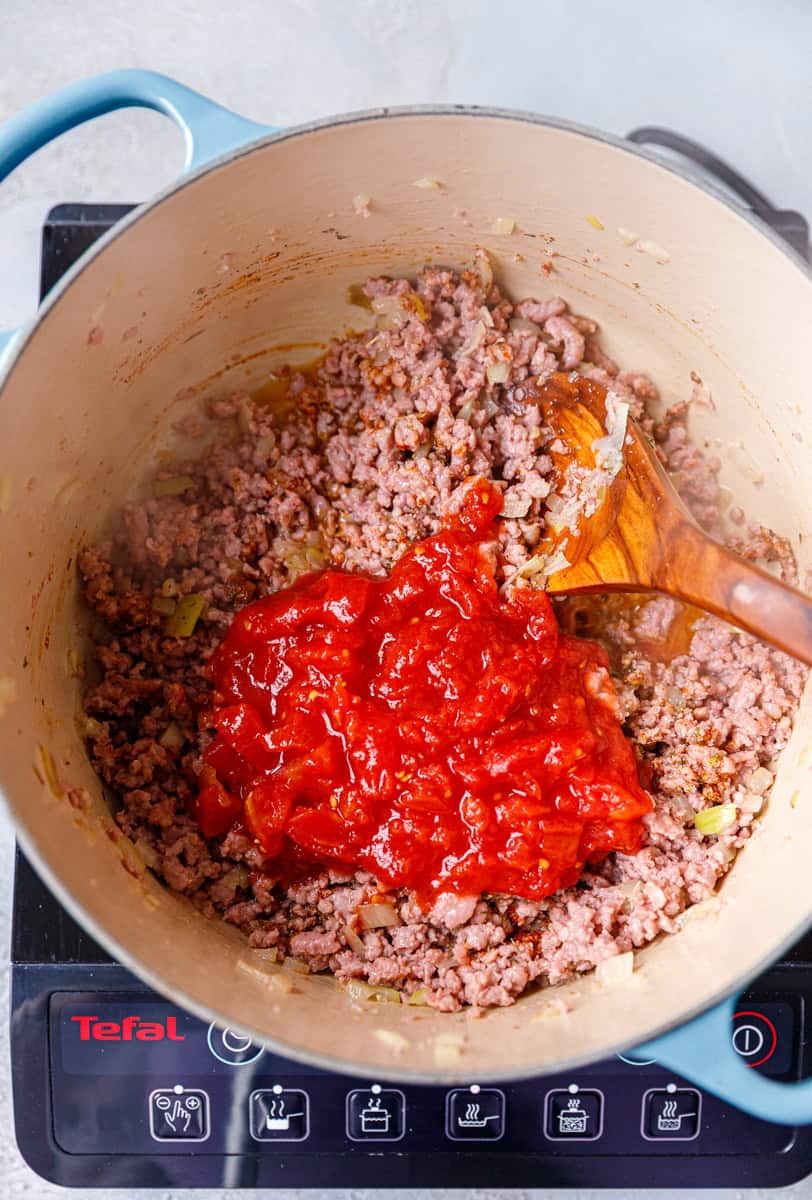 A cooking pot with browned ground beed, seasoning and crushed tomatoes.