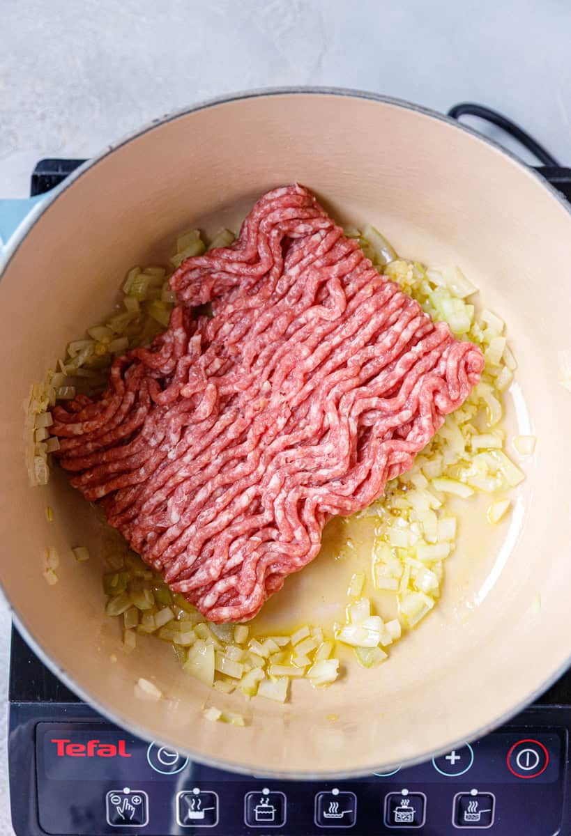 Ground beef added to sautéed onions in a Dutch oven to start making Keto Cabbage Roll Soup. The onions are softened in olive oil for a rich base flavor.
